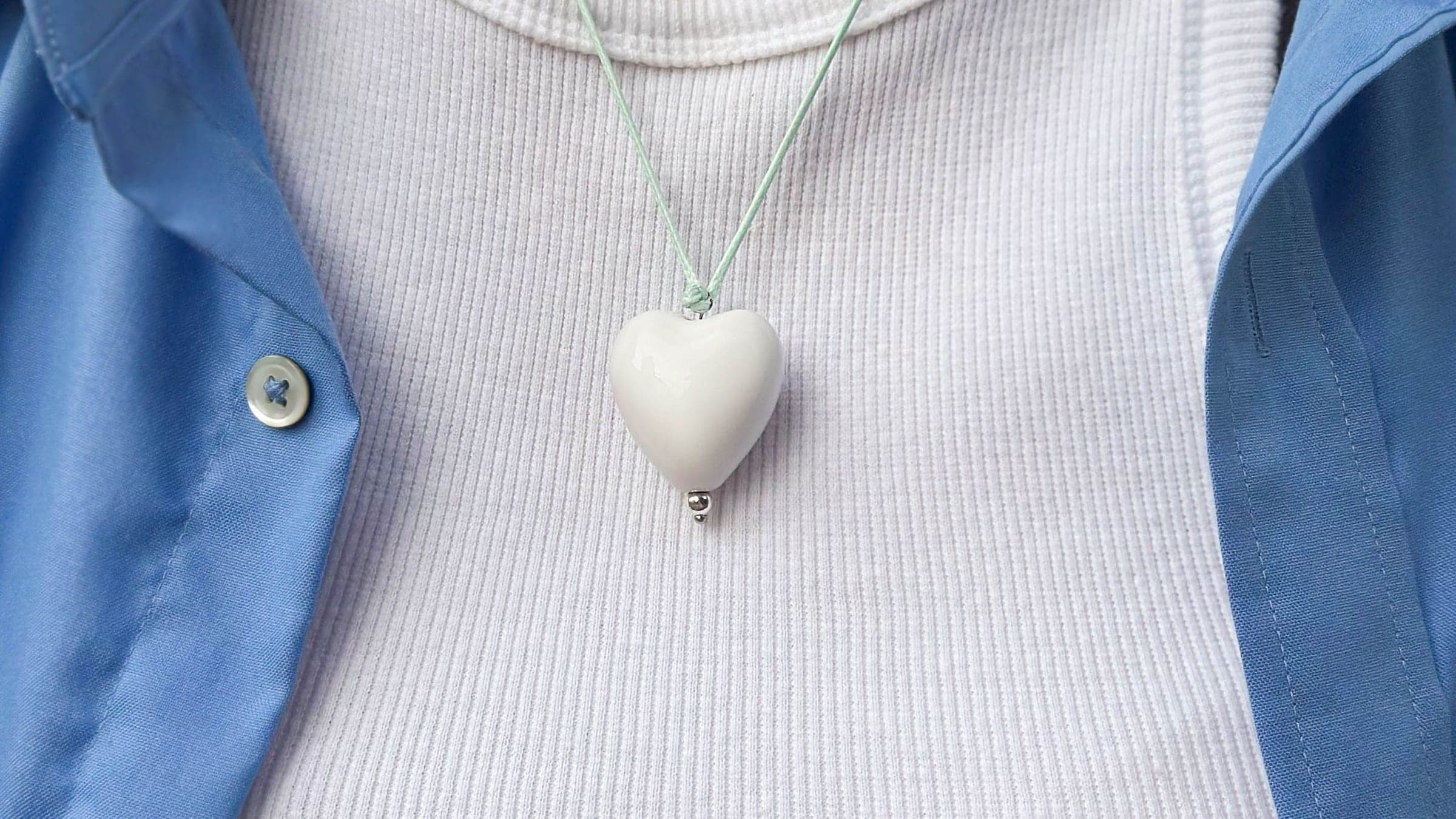 A pale heart-shaped pendant made with ashes, worn on a fine cord over a white top