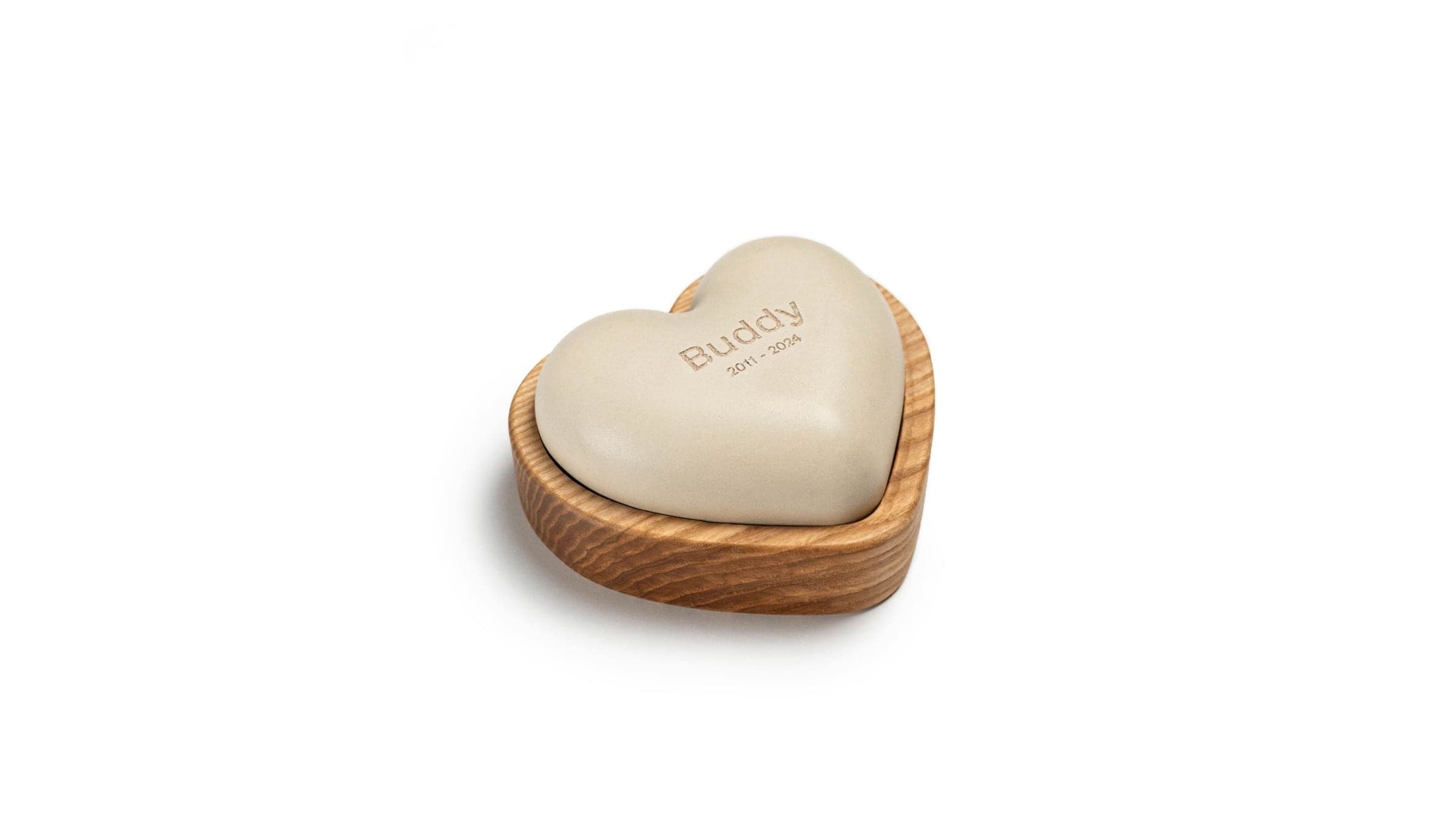 A cream heart-shaped remembrance stone engraved "Buddy", resting in a carved wooden base